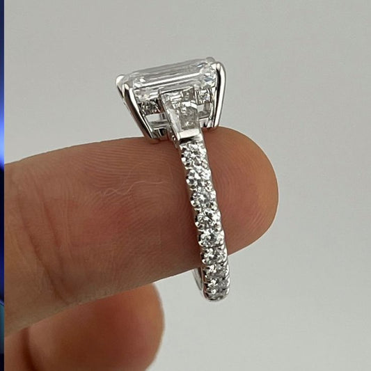 Custom emerald cut diamond ring with baguette side stones and diamond pavé split shank band held between fingers, made to order in 18k white gold in Dubai UAE by Lamae Jewelry